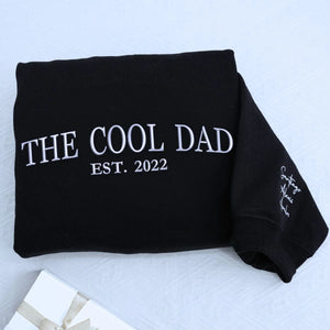 Black The Cool Dad Sweatshirt with EST. 2022 embroidery and kid name on sleeve, a meaningful and cozy gift for dad