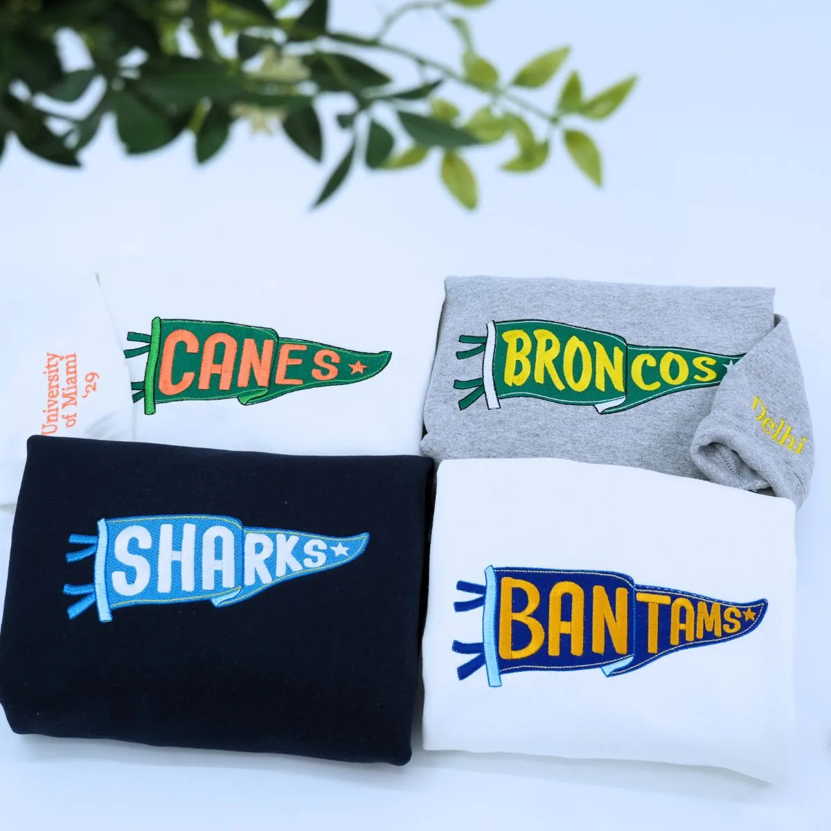 Custom embroidered white sport gray and black pennant sweatshirts folded on table – personalized team name hoodies for school spirit, game day, and sports fans