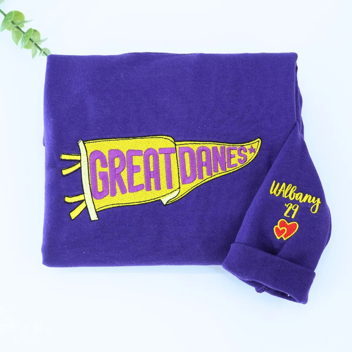 Custom embroidered purple pennant sweatshirt folded on table – personalized team name sweatshirt for school spirit, game day, and sports fans