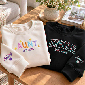 Matching sand Aunt and black Uncle embroidered sweatshirts with personalized sleeves, a gift for a new aunt and uncle at a baby shower.