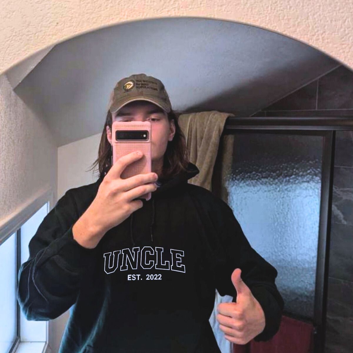 Man taking a mirror selfie wearing a black 'Uncle Est. 2022' hoodie, casual and cozy outfit.