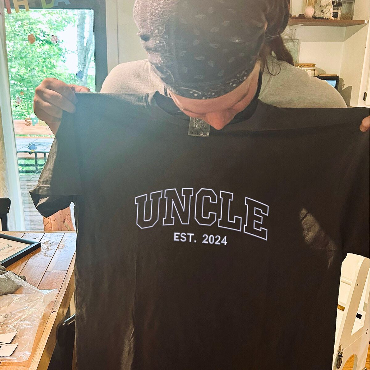 Person holding up a black 'Uncle Est. 2024' embroidered T-shirt, a great gift idea.