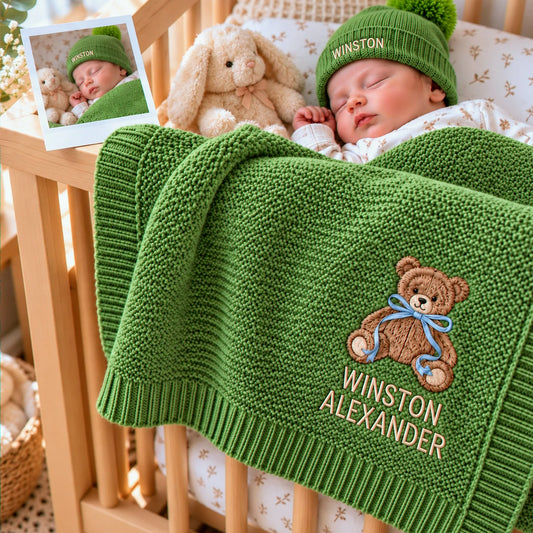Sleeping baby with a personalized green knit blanket featuring teddy bear embroidery and a matching name beanie