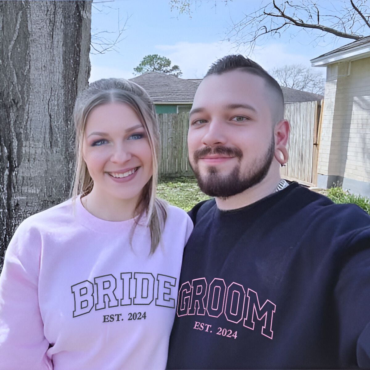 Engaged couple wearing matching 'Bride' and 'Groom' sweatshirts in an outdoor photoshoot.