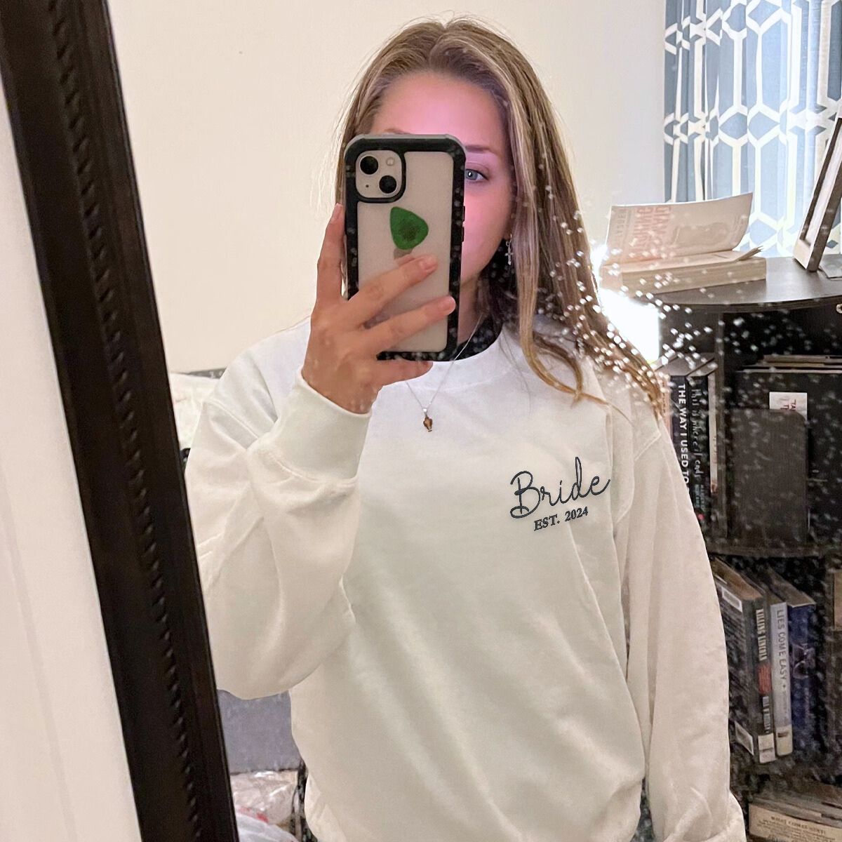 Bride wearing a white 'Bride Est. 2024' sweatshirt, taking a selfie in her bedroom.