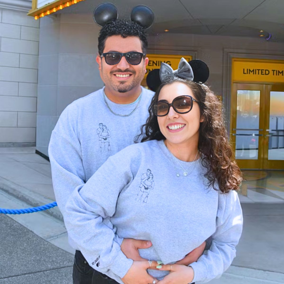 Joyful couple in matching gray Embroly hoodies with custom portrait embroidery, sharing a special moment at a theme park.