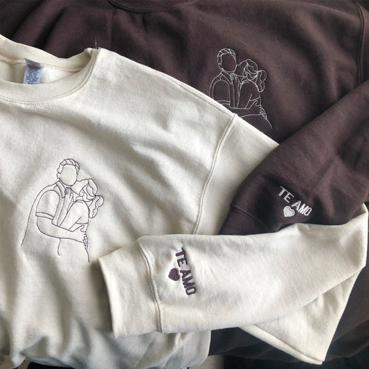 Cream and brown sweatshirts with hand-drawn couple portrait embroidery and "Te Amo" heart detail on the cuff
