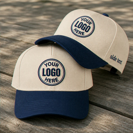 Two customizable baseball caps with cream panels and navy blue visors, displayed on a weathered wooden surface. The front cap shows a circular embroidered logo placeholder on the front panel and side text on the side of the visor, while the rear cap shows the back side with a matching navy crown and visor.