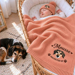 Sleeping baby beside the family dog with a coral knit blanket embroidered with the dog’s portrait and “Protected By”, a personalized gift for expectant parents.