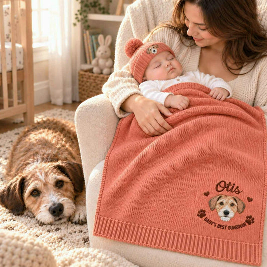 Mother holding a sleeping baby under a coral knit blanket embroidered with the family dog’s portrait, a personalized baby shower gift for dog lovers.