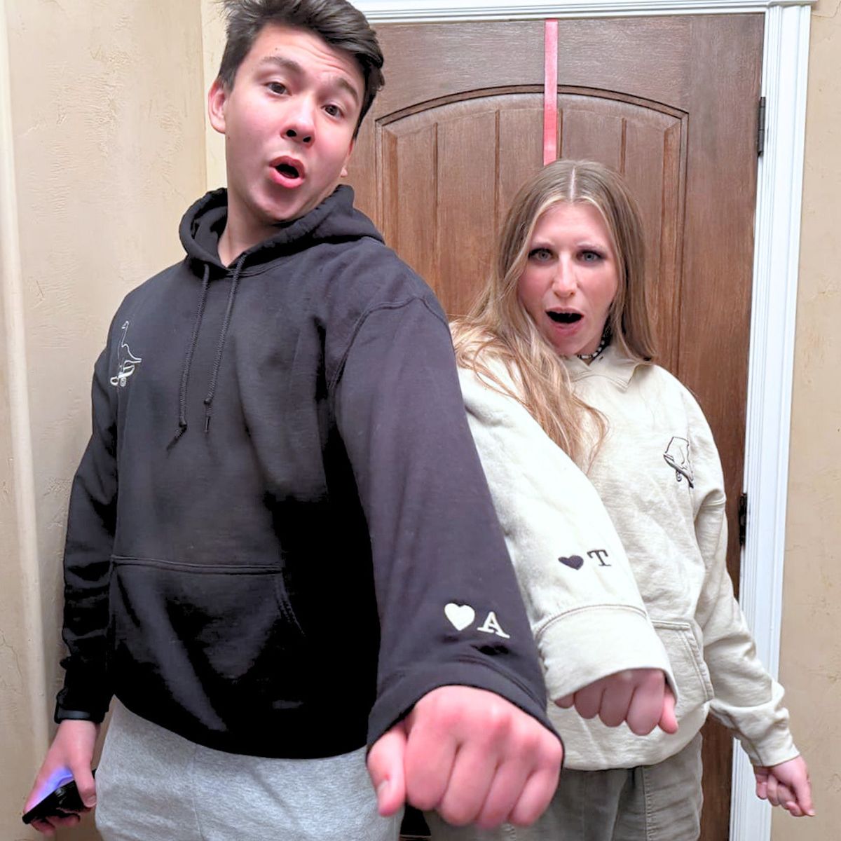 Fun-loving couple showing off their black and beige Embroly hoodies with custom embroidered initials on sleeves.