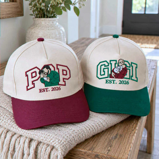 A pair of personalized baseball caps designed for a new grandparent reveal, featuring embroidered names and illustrations of a grandfather and a grandmother with a baby. This cute product is an ideal way to announce a pregnancy to future grandparents in 2026.