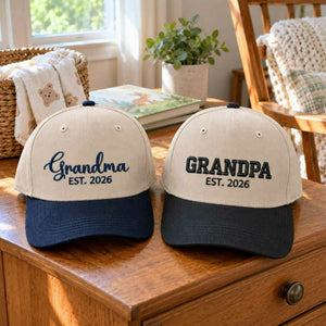Custom embroidered Grandma and Grandpa Est. 2026 baseball caps set, personalized gifts for new grandparents on a wooden table with cozy background.