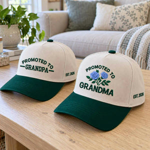 Matching Promoted to Grandma and Promoted to Grandpa Est 2026 embroidered baseball caps on a wooden table