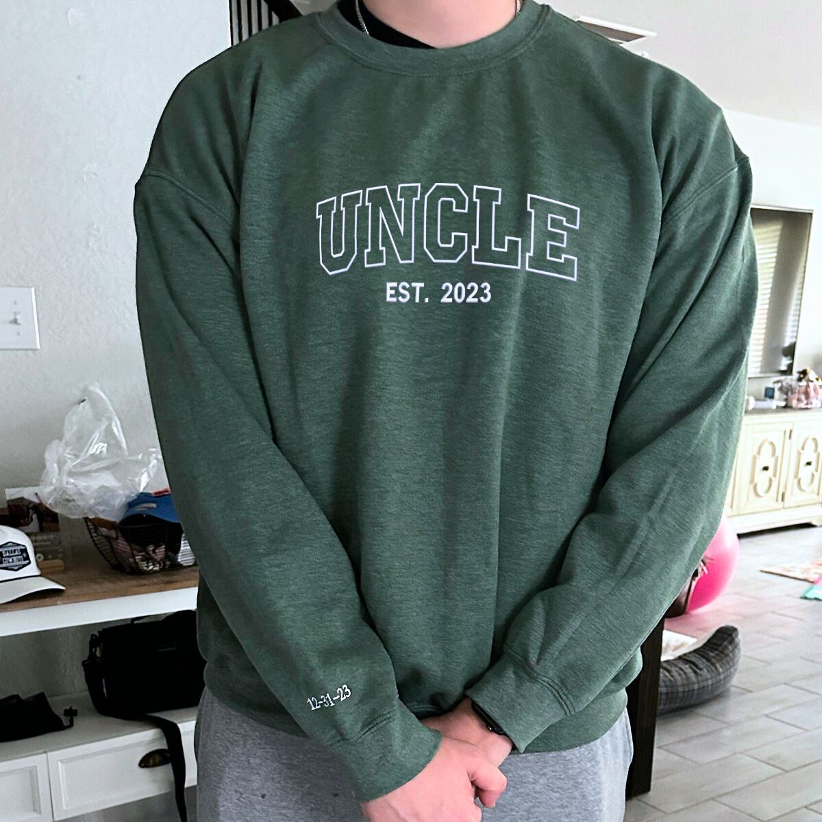 Man wearing a green 'Uncle Est. 2023' embroidered sweatshirt, a trendy casual outfit.