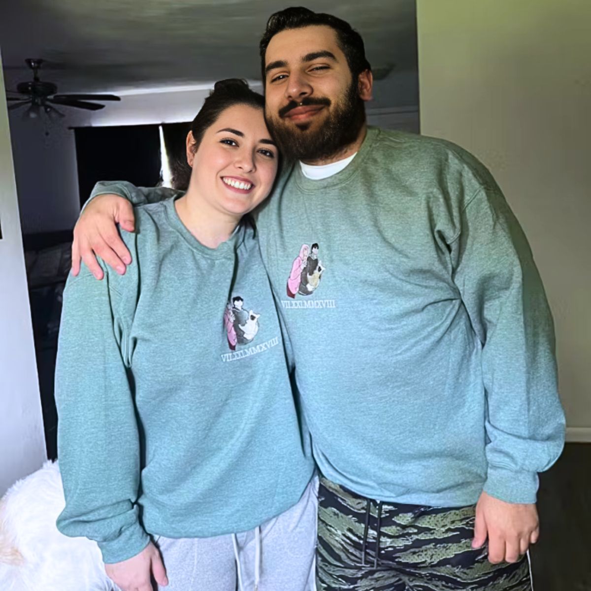 Smiling couple wearing matching green Embroly sweatshirts with personalized embroidery, celebrating their love.