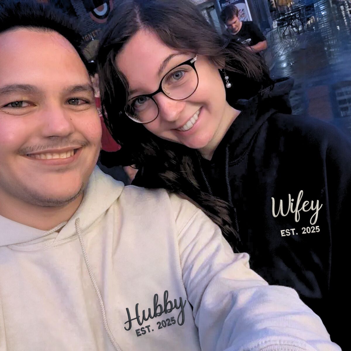 Couple wearing matching 'Hubby EST. 2025' and 'Wifey EST. 2025' hoodies, a perfect gift for newlyweds or anniversaries.