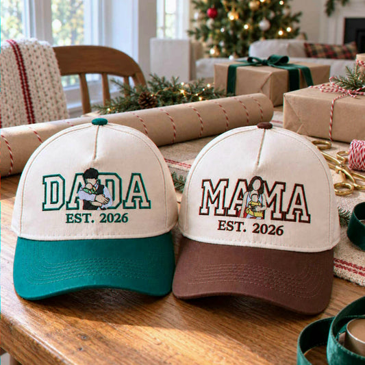 "Embroidered 'Dada est. 2026' and 'Mama est. 2026' two-tone baseball caps with parent and baby illustrations, set on a wooden table with Christmas gift wrapping and a decorated tree background. Custom family announcement gift idea.