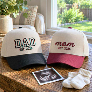 Matching embroidered Mom and Dad caps with maroon and black brims beside a family photo, a baby announcement gift for new parents