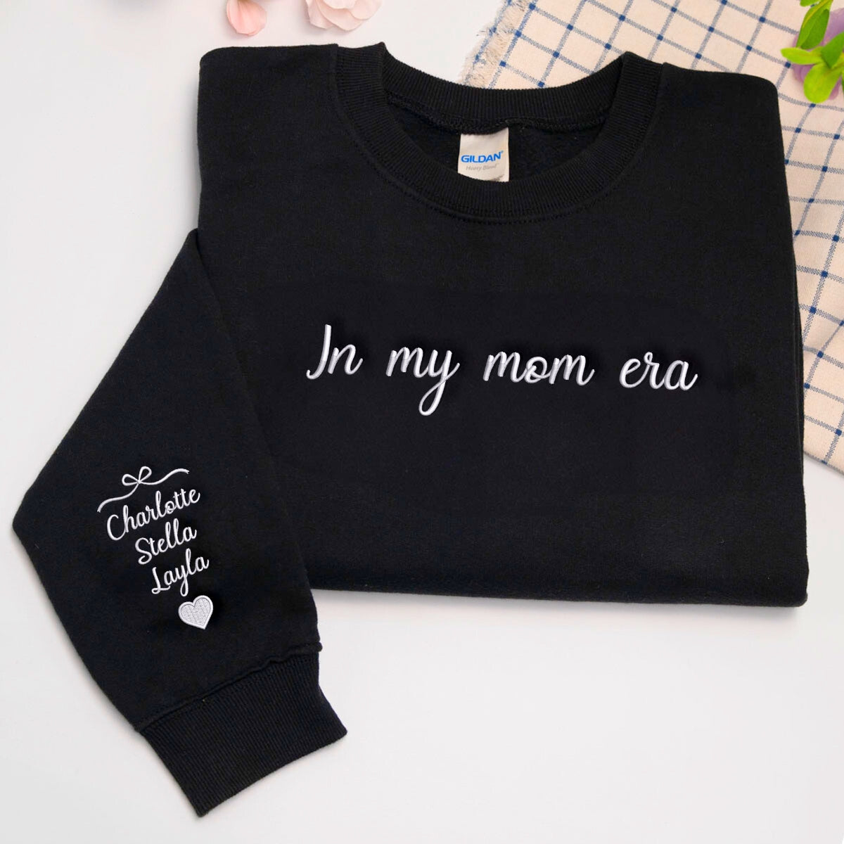 Black embroidered sweatshirt with 'In my mom era' text and personalized children's names on the sleeve.