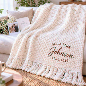 Cream waffle blanket with brown Mr. & Mrs. Johnson embroidery and personalized wedding date, draped over a sofa.