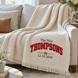 Cream waffle blanket with personalized red glitter THOMPSONS embroidery and wedding date, draped over a sofa.