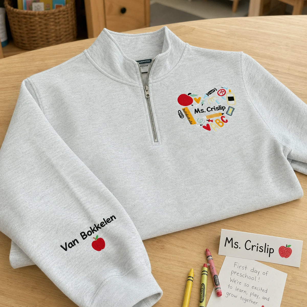 Heather gray quarter-zip featuring Ms. Crislip with a colorful classroom heart on the chest and personalized text icon on the sleeve
