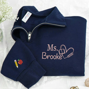 Navy teacher quarter-zip with personalized name, book-and-pencil heart on the chest and apple and pencil sleeve embroidery