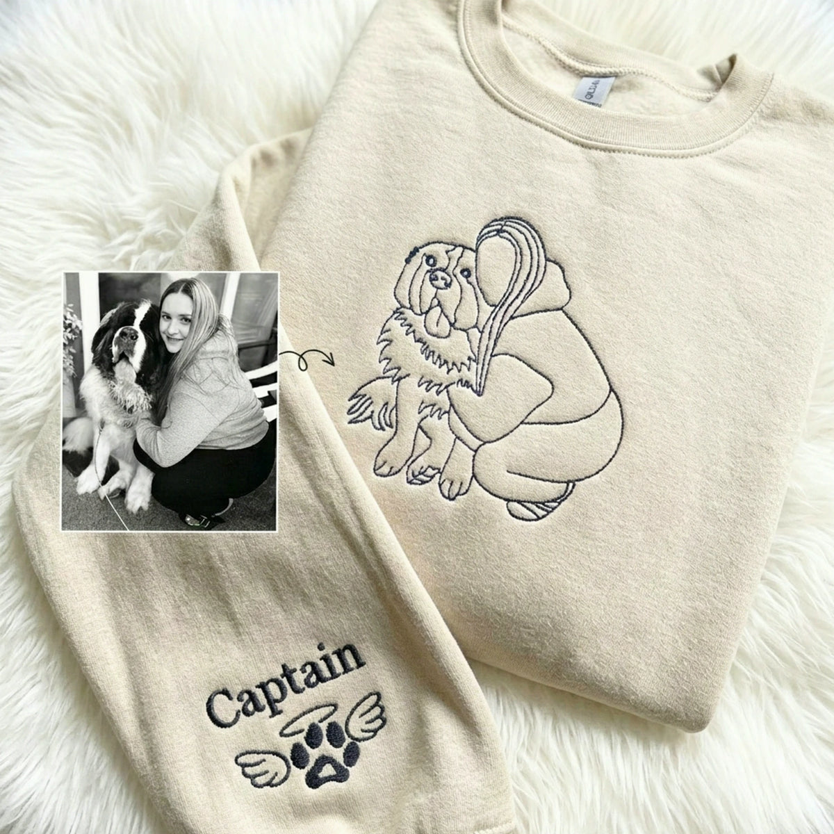 Cream sweatshirt with line-art embroidery of woman hugging dog, name and winged paw stitched on sleeve