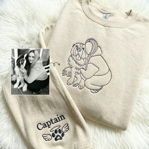 Cream sweatshirt with line-art embroidery of woman hugging dog, name and winged paw stitched on sleeve