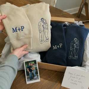 Hand unboxing beige and navy sweatshirts with initials and full-body couple portrait embroidery, photo and note inside box