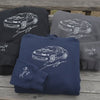 Close-up video of black, grey and navy car-embroidered sweatshirts, a hand touching the stitched car design and cuff message, soft background music