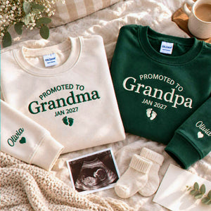 Sand and forest green Promoted to Grandma and Grandpa embroidered sweatshirts beside an ultrasound photo, a pregnancy announcement gift for grandparents-to-be.