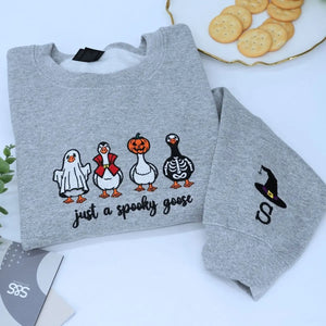 Funny spooky goose embroidered Halloween sweatshirt on flatlay with fall decorations