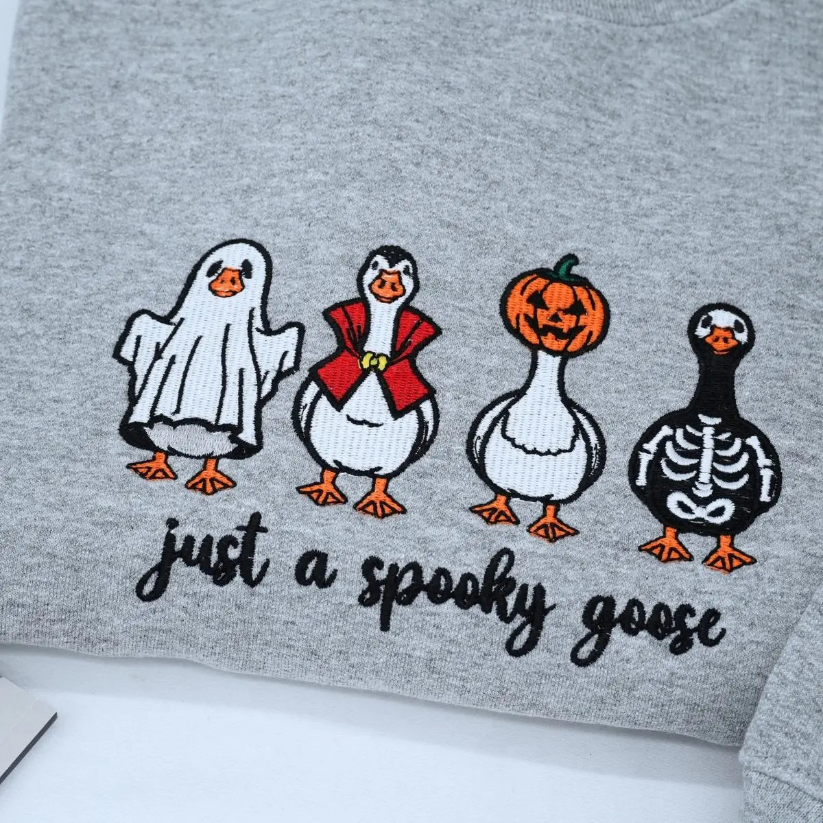 Funny spooky goose embroidered Halloween sweatshirt on flatlay with fall decorations
