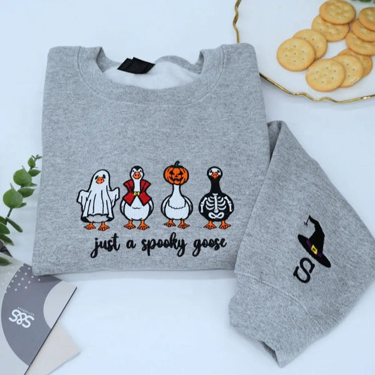 Funny spooky goose embroidered Halloween sweatshirt on flatlay with fall decorations