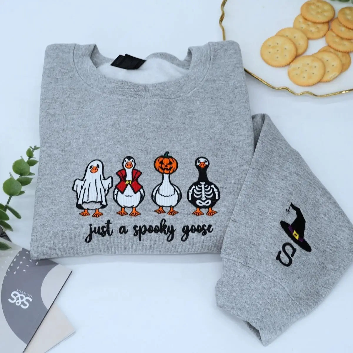 Funny spooky goose embroidered Halloween sweatshirt on flatlay with fall decorations