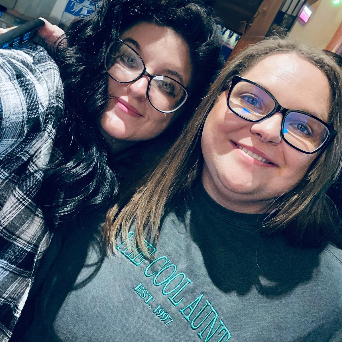 Two women with glasses posing together, one wearing a dark gray 