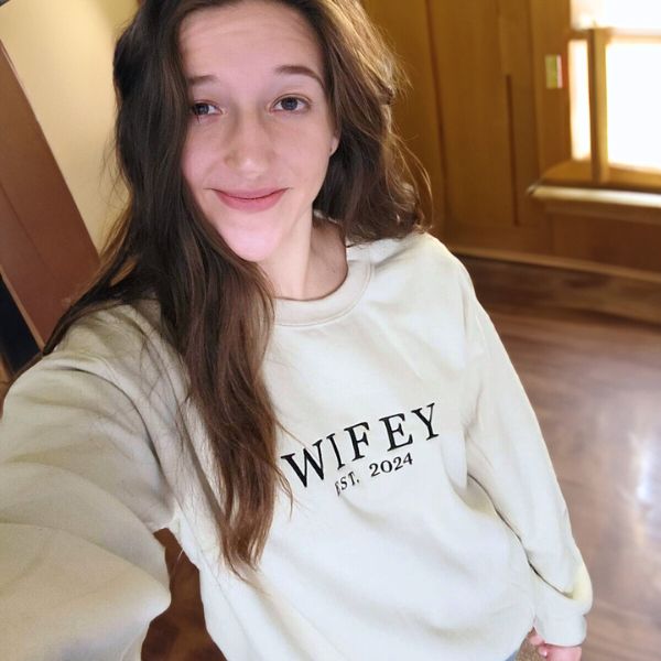 Woman wearing a sand 'Wifey Est. 2024' embroidered sweatshirt.