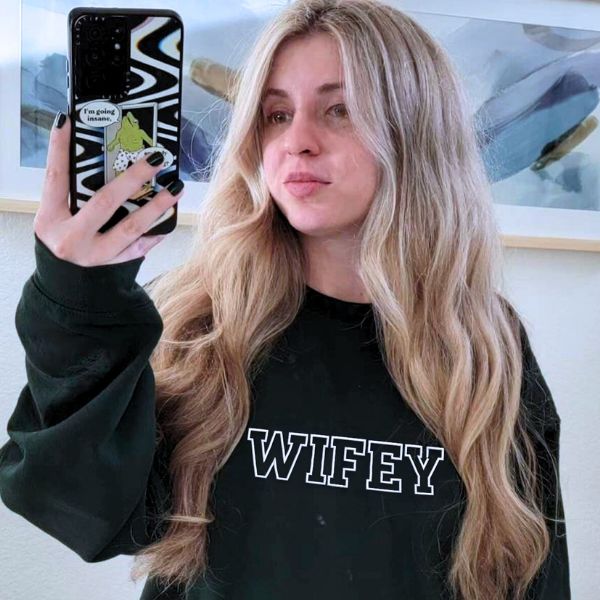 Woman in dark green 'Wifey' sweatshirt taking a mirror selfie, showcasing bold lettering.