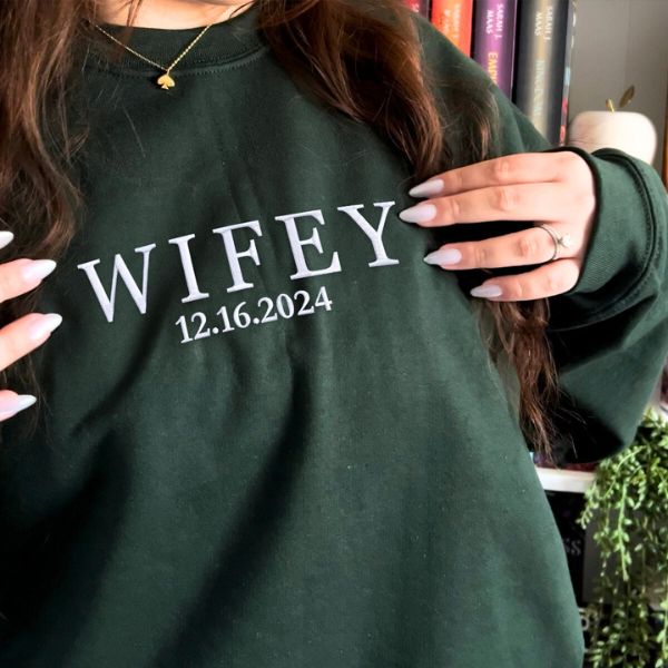 Dark green 'Wifey' sweatshirt with custom date embroidery, hands highlighting the design.