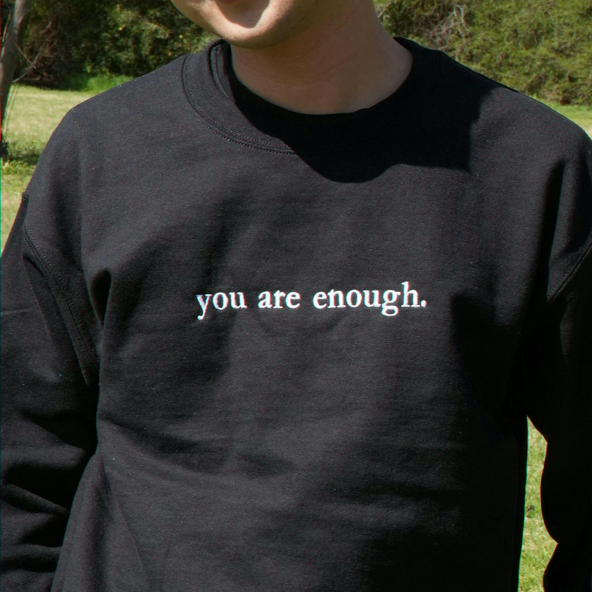 Person wearing a black sweatshirt with 'you are enough' text outdoors.