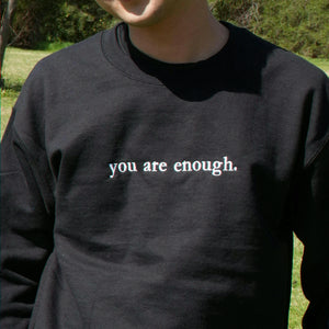 Person wearing a black sweatshirt with 'you are enough' text outdoors.