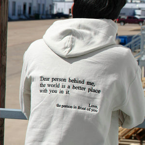 Person wearing a white hoodie with a message on the back, standing outdoors.